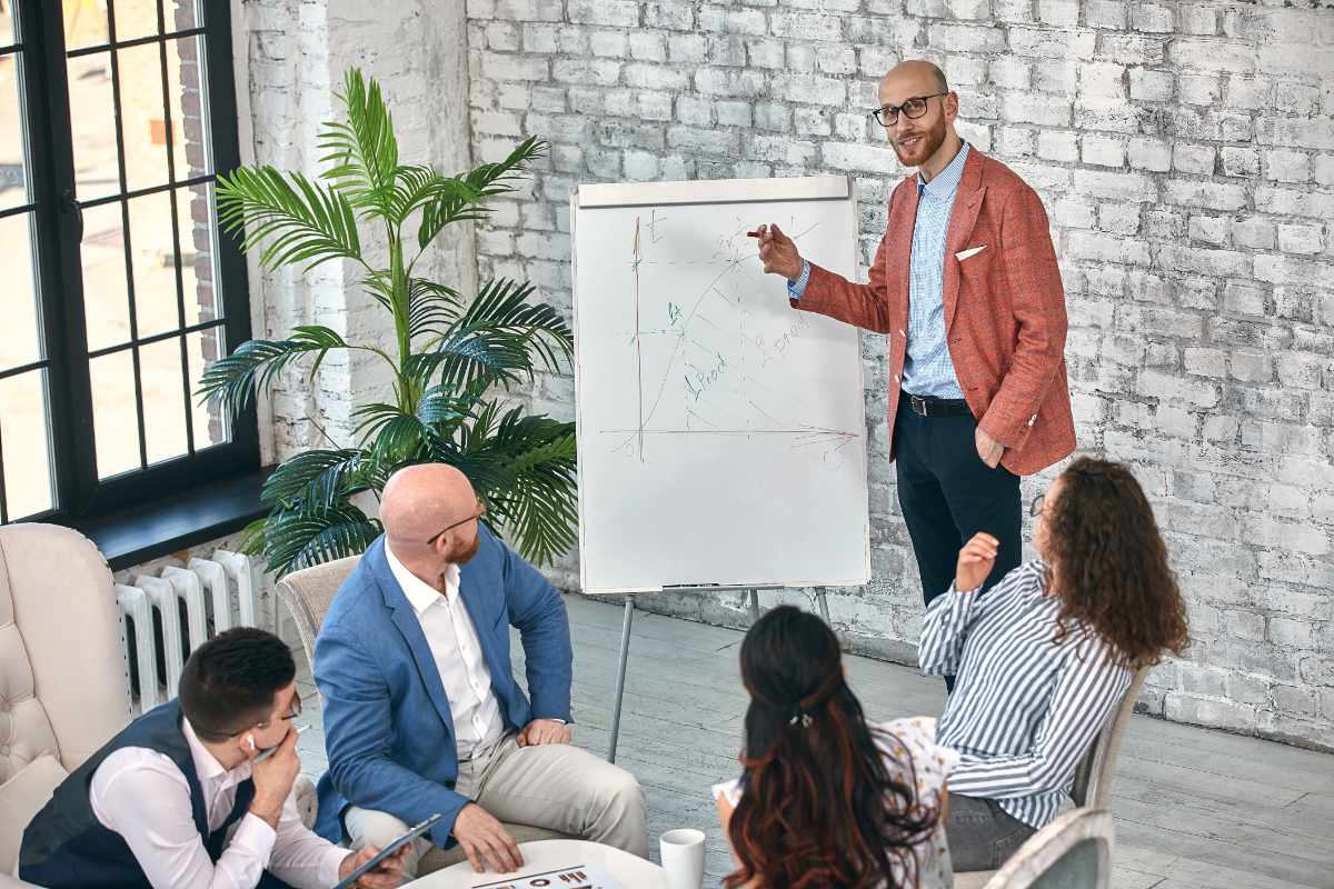 Confident businessman writing on flip charts presentation new project in boardroom at company meeting. Serious mentor auditor speaks with partners about business using board and graphs. selective focus